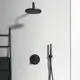 Schwarze Duschelemente von Ideal Standard an einer hellen Wand, einschließlich einer großen Regendusche, einem Handbrausehalter und einem Thermostat. Handtuch auf einem schwarzen Gestell.
